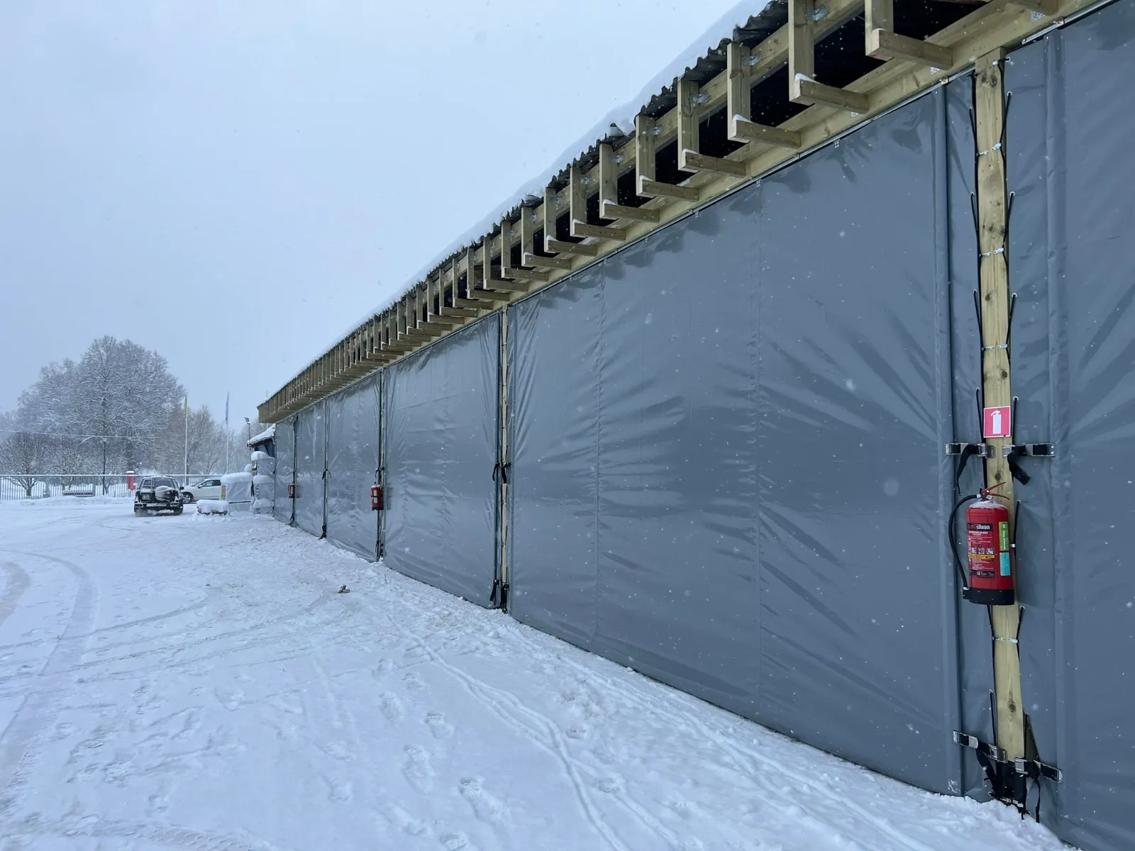 Pelēkas PVC sienas garai koka konstrukcijas nojumei ziemā sniegā